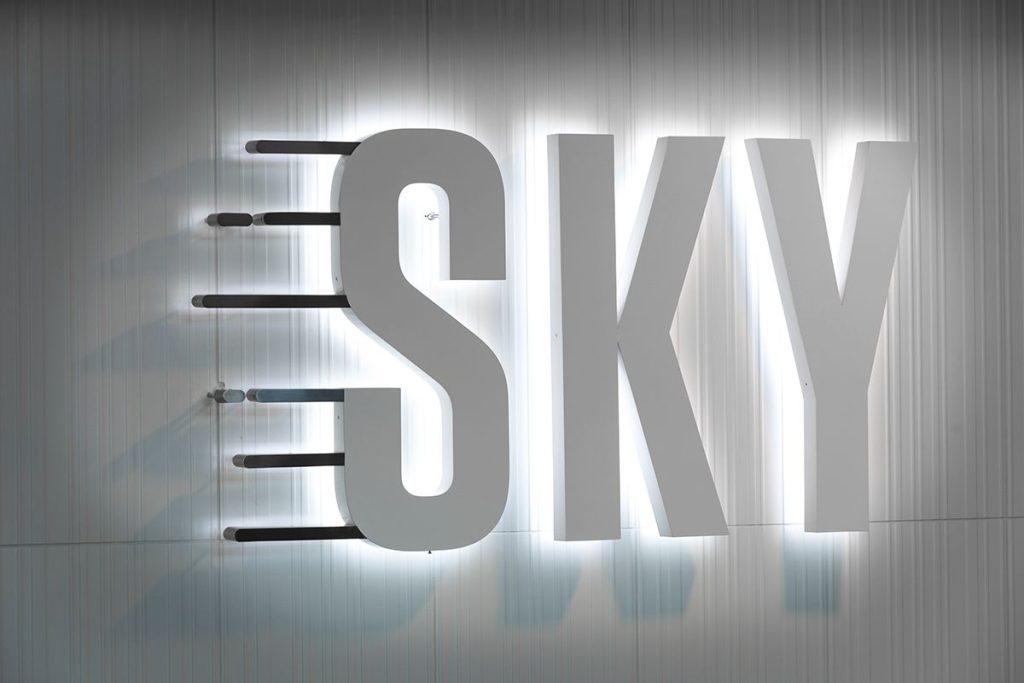 Illuminated 3D sign displaying the word "SKY" against a textured wall.