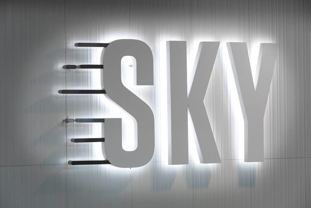 Illuminated sign spelling "SKY" with trailing lines on a gray wall.