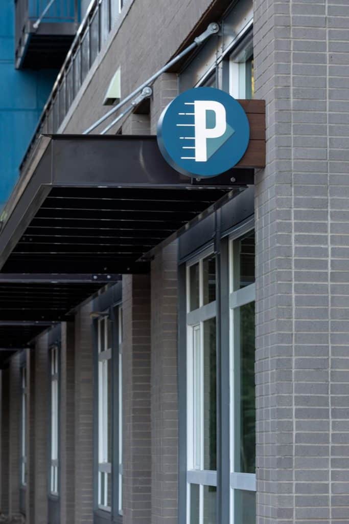 A building exterior with a black awning and a blue circular sign featuring a white "P" logo.