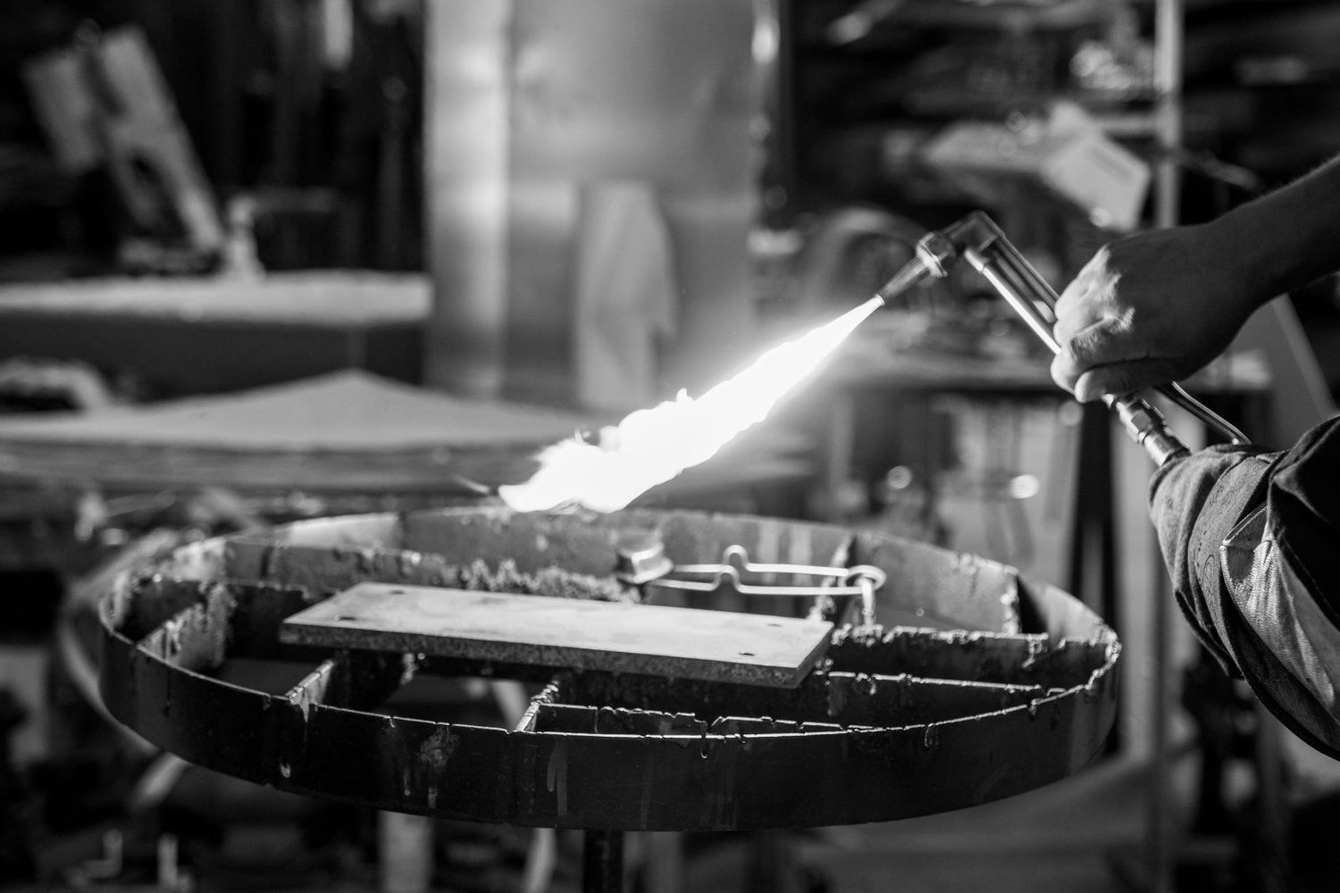 A person uses a blowtorch to heat a metal object on a circular workbench in a workshop.