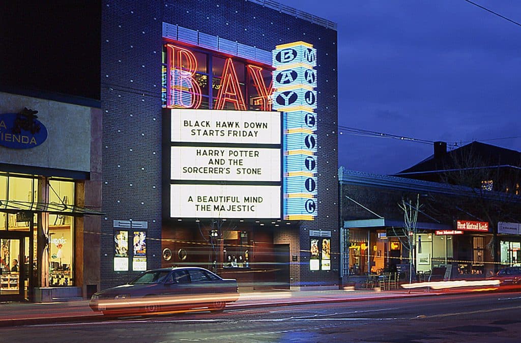 Lit cinema marquee at night displaying movie titles: "Black Hawk Down," "Harry Potter and the Sorcerer's Stone," "A Beautiful Mind," and "The Majestic.