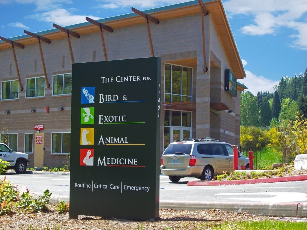 Sign for "The Center for Bird & Exotic Animal Medicine" outside a brick building with cars parked nearby.