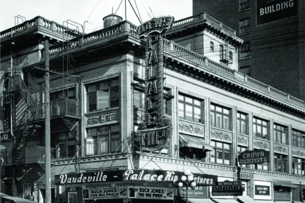 Black and white image of a historic theater building with "Vaudeville" and "Palace Hipp" signage. Pedestrians and vintage cars are visible on the street.