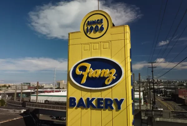 Tall yellow sign for Franz Bakery, established in 1906, with industrial background and road nearby.