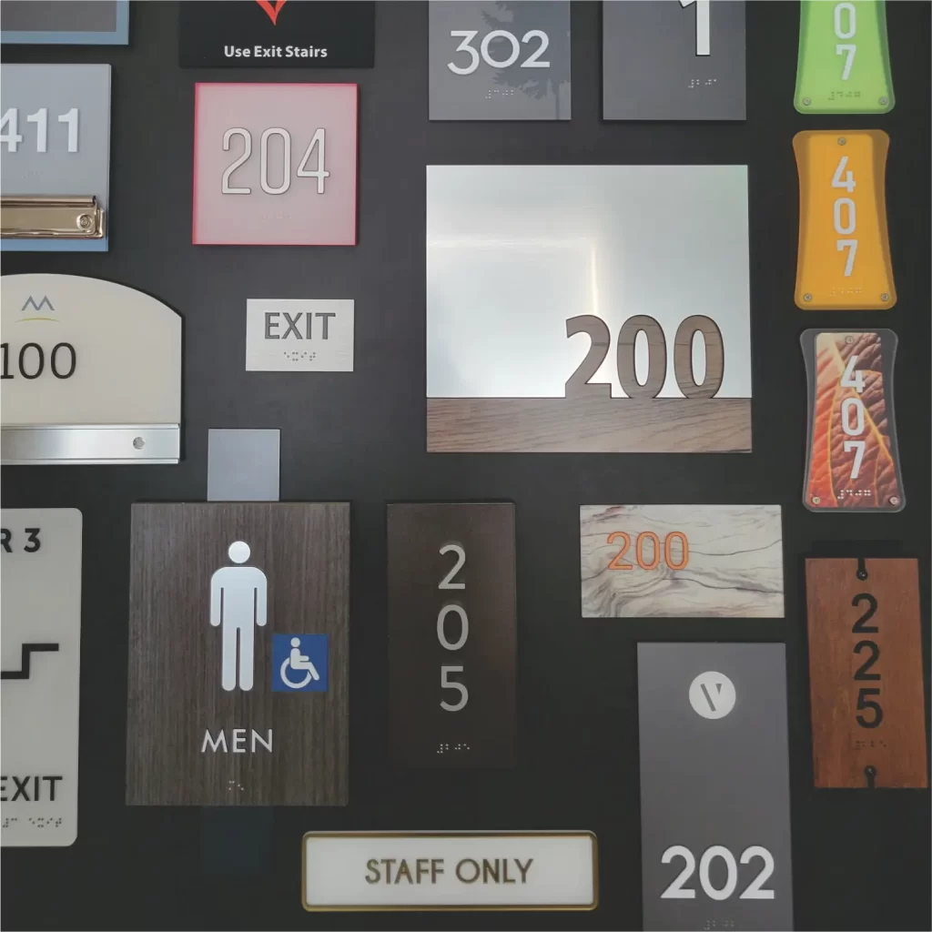 A display of various room number and exit signs, including "200," "204," "202," "407," "EXIT," and "STAFF ONLY," mounted on a wall.