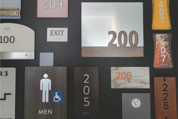 A display of various room number and exit signs, including "200," "204," "202," "407," "EXIT," and "STAFF ONLY," mounted on a wall.