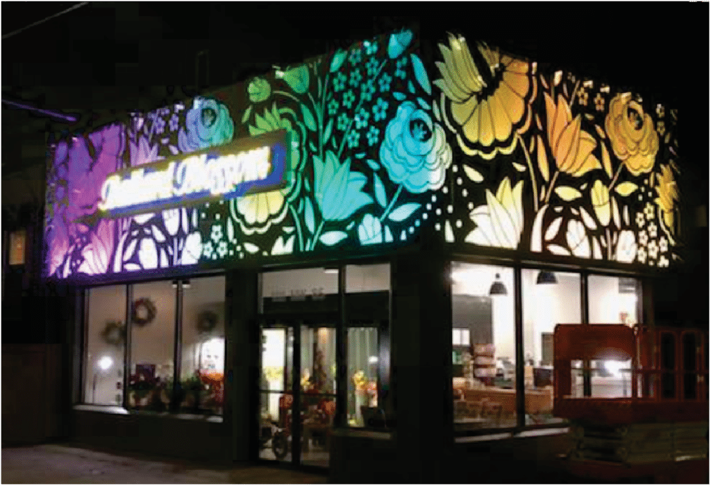 A flower shop at night with a colorful, illuminated floral design across its upper facade.