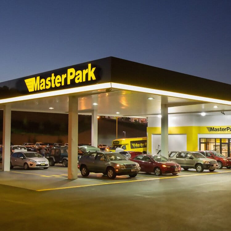 Parking lot at night with several cars parked under a lit canopy displaying a "Master Park" sign.