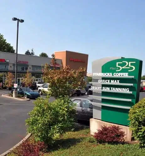 Shopping plaza with Starbucks Coffee, Office Max, and Desert Sun Tanning. Parking lot with several cars and a tall sign displaying the business names.