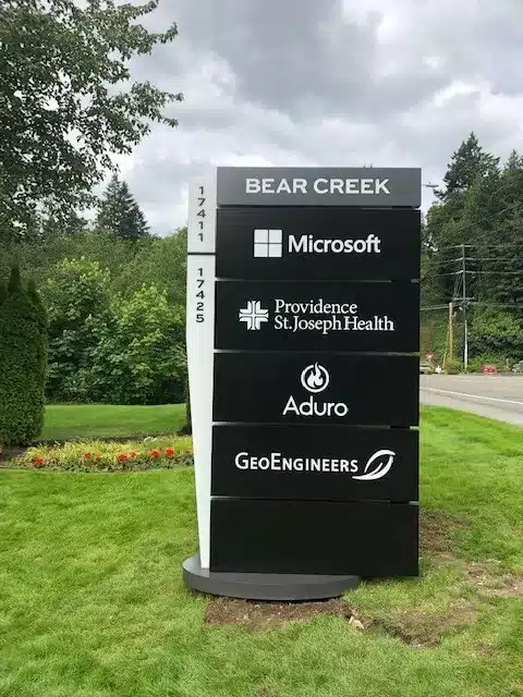 Outdoor sign listing businesses at Bear Creek: Microsoft, Providence St. Joseph Health, Aduro, and GeoEngineers. Surrounded by trees and grass.