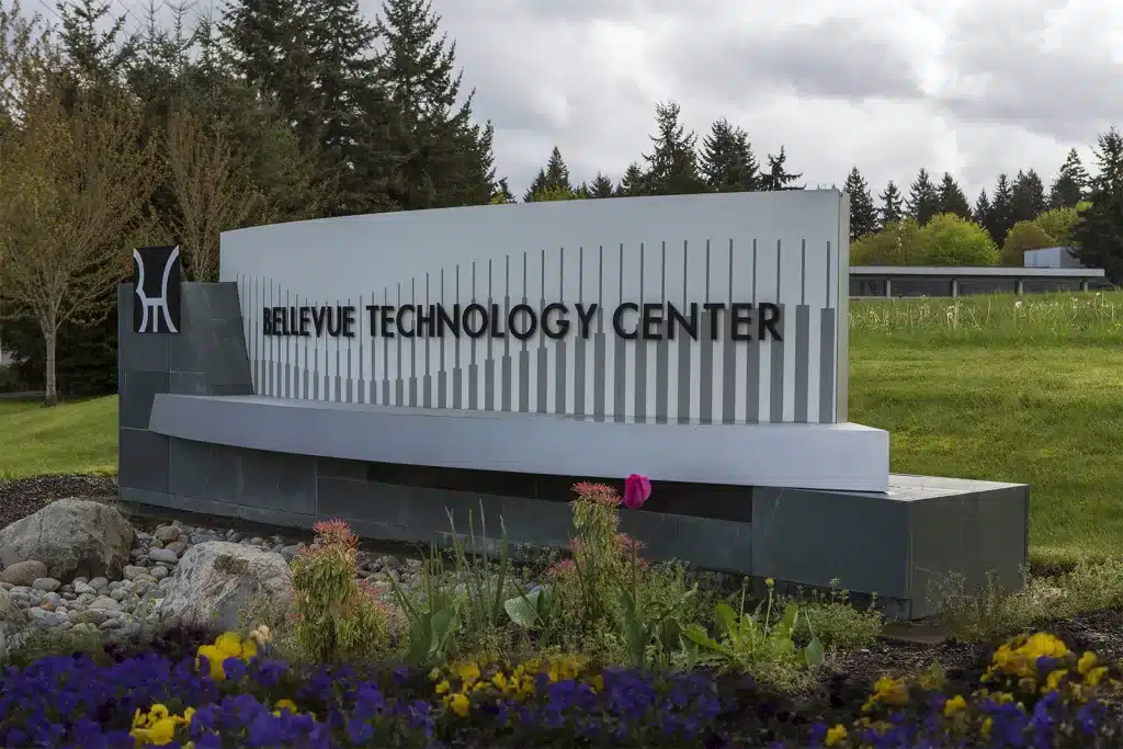 Sign for Bellevue Technology Center surrounded by rocks, flowers, and trees, under a cloudy sky.