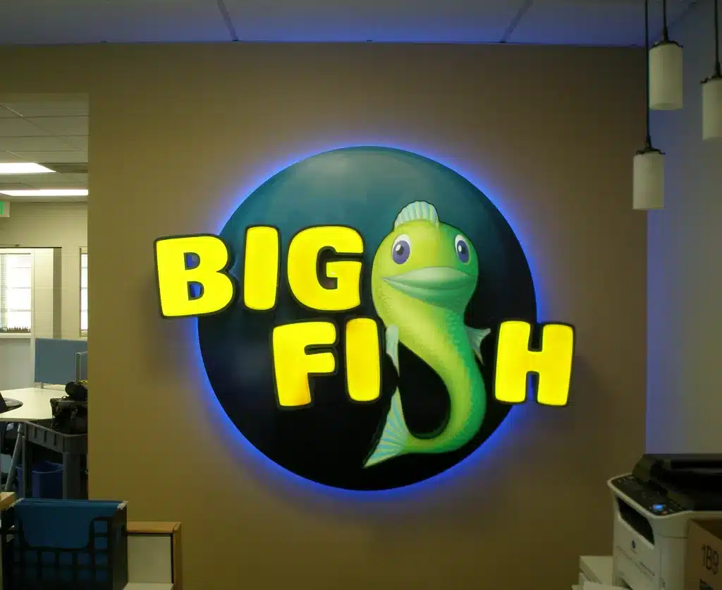 Illuminated "Big Fish" sign with a cartoon fish against a circular blue background on a beige wall.