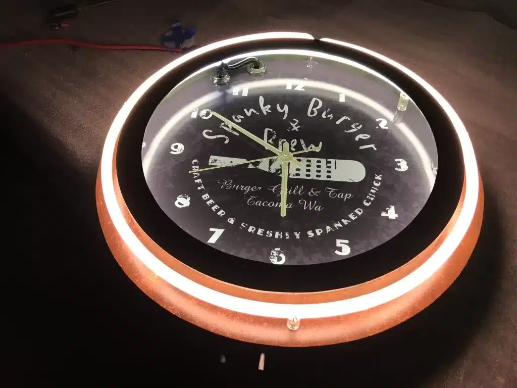 A round illuminated wall clock with "Swanky Burger & Brew" on the face, displaying a knife, fork, and restaurant details from Tacoma, WA. The clock reads 12:07.