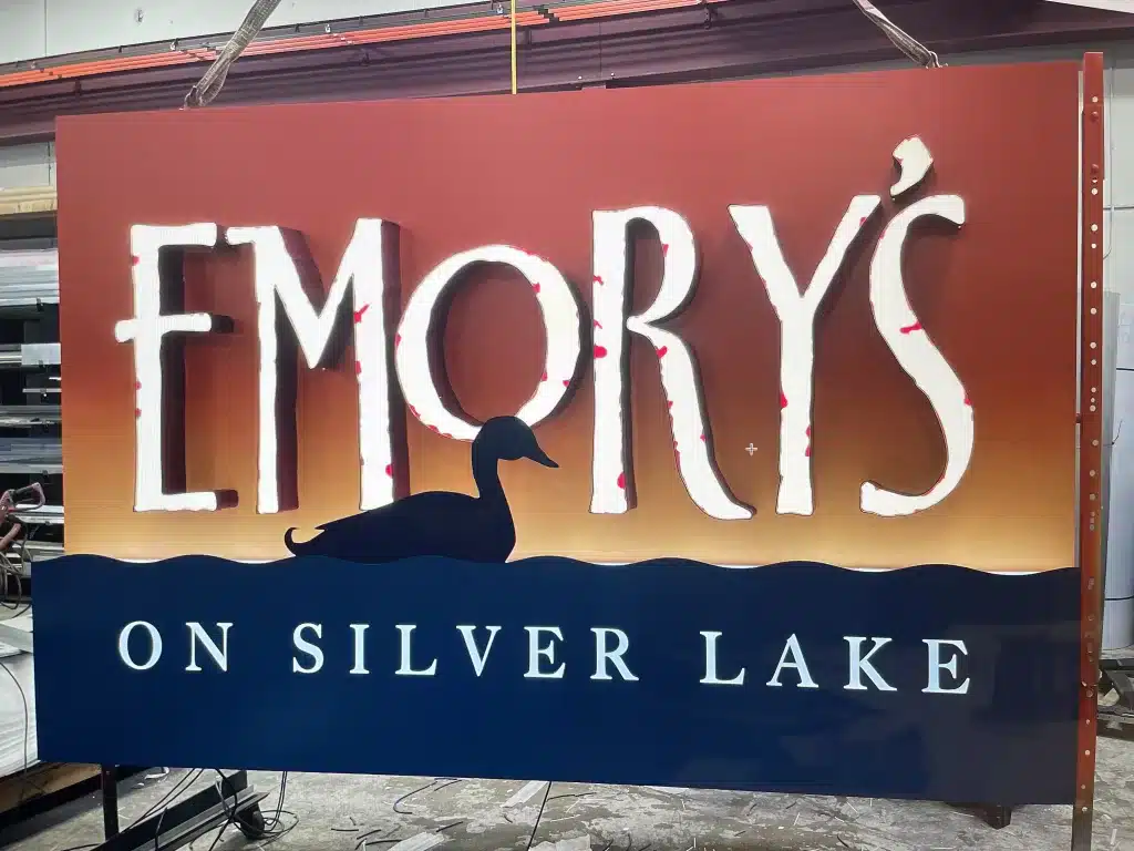 A sign for "Emory's on Silver Lake" featuring large text and a duck silhouette against a sunset background.