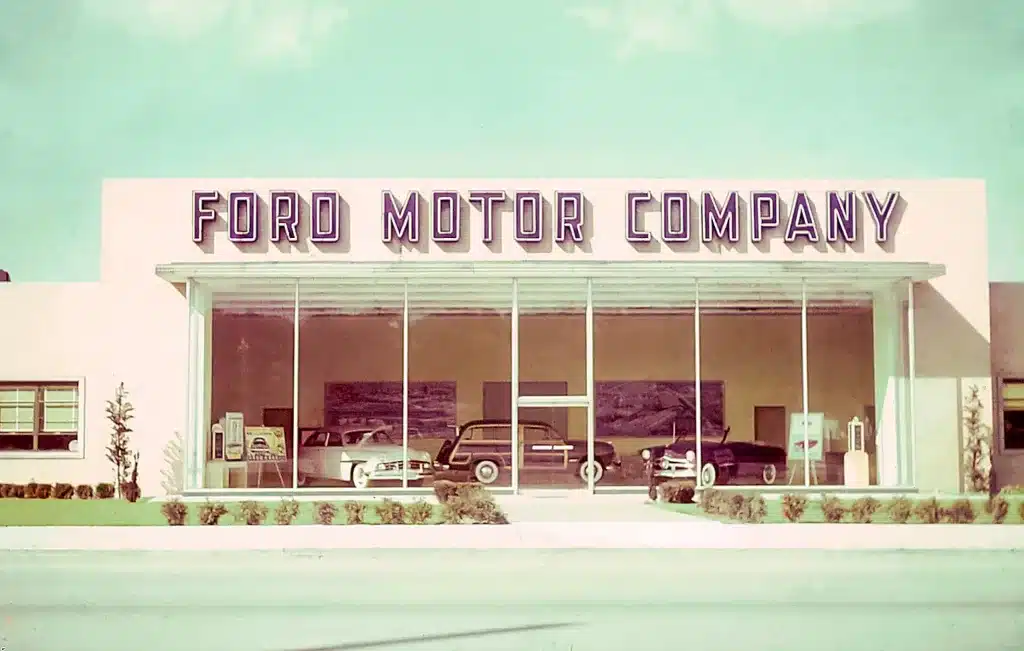 Vintage Ford Motor Company dealership with cars displayed through large glass windows in a 1960s architectural style.