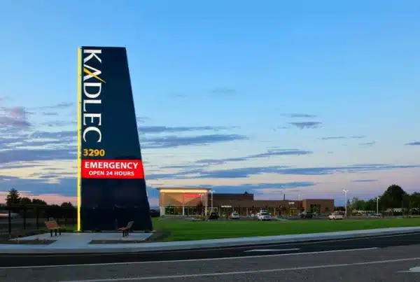 Kadlec hospital with a tall sign indicating 24-hour emergency services, set against a sunset sky.