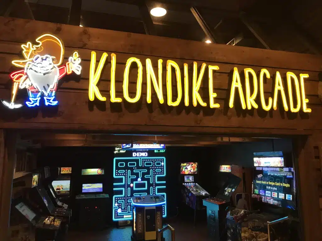 Entrance of Klondike Arcade with neon yellow sign and visible arcade games inside, including a Pac-Man machine.