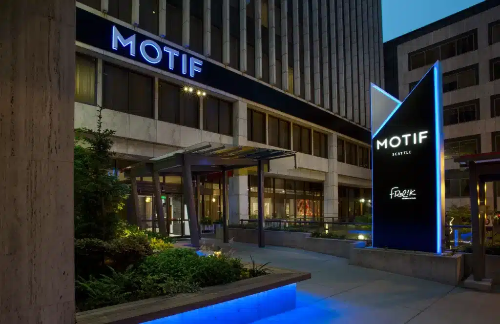 Hotel entrance with a large sign that reads "Motif Seattle" next to a garden area and modern building facade.