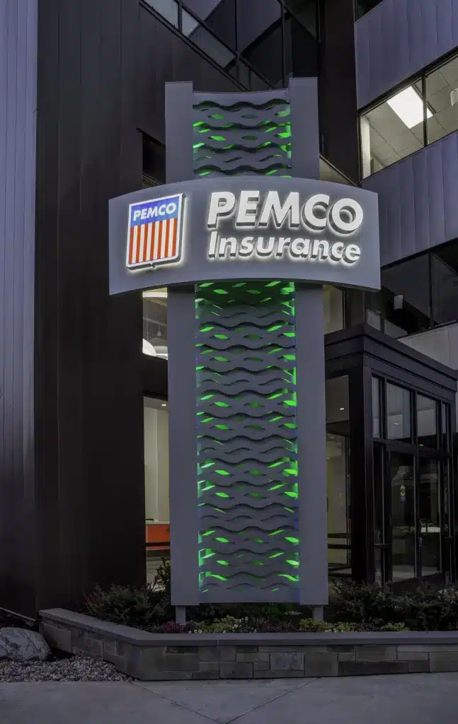 Outdoor sign for PEMCO Insurance with illuminated logo and green wave patterns, situated in front of a modern building.