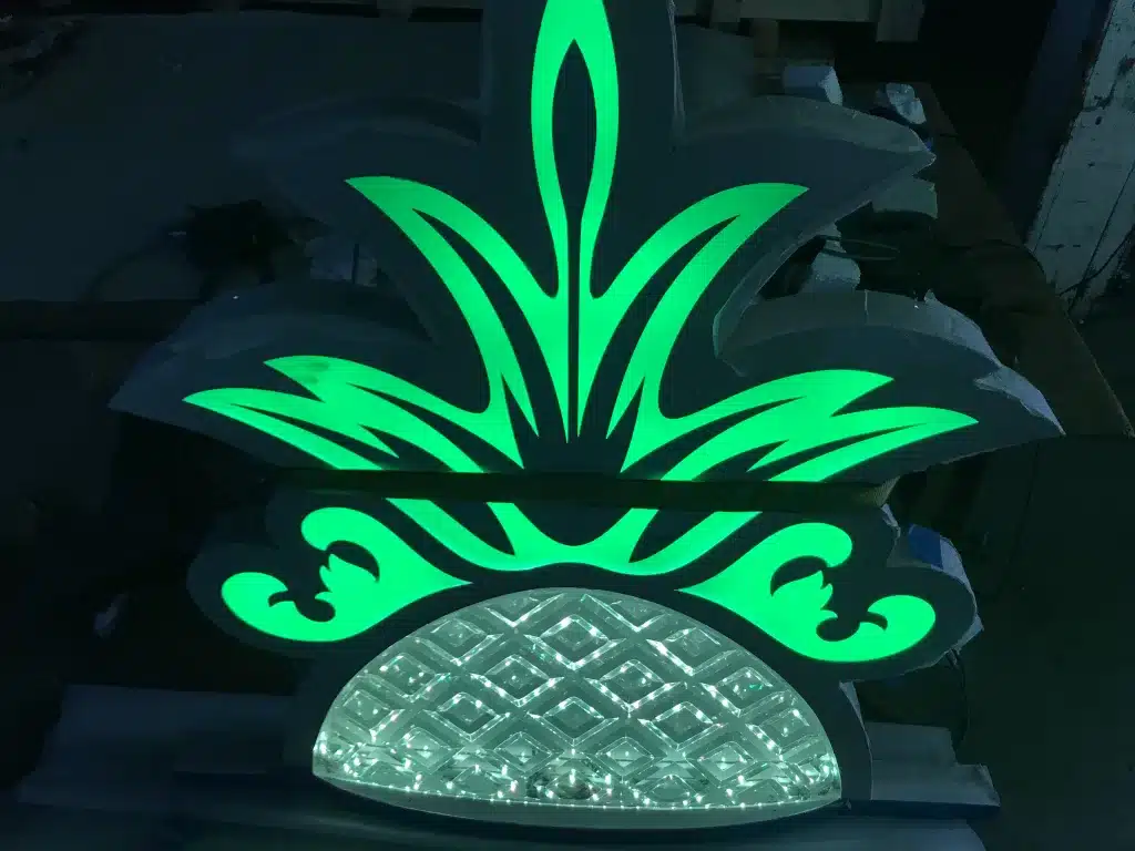 Illuminated decorative sign with a green, stylized pineapple design on a dark background.