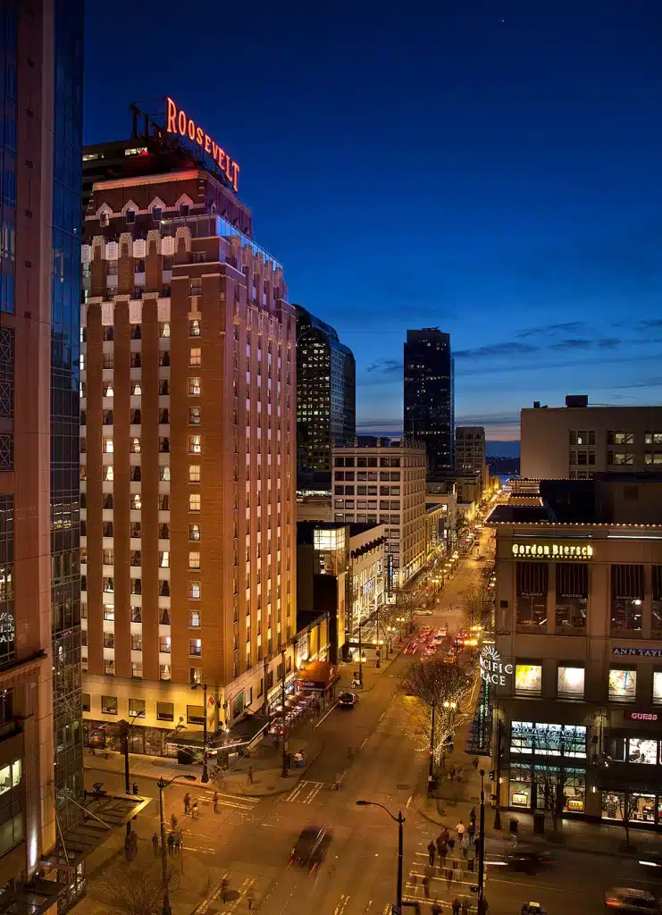 Night view of a city street with the illuminated Roosevelt Hotel on the left and various buildings alongside.