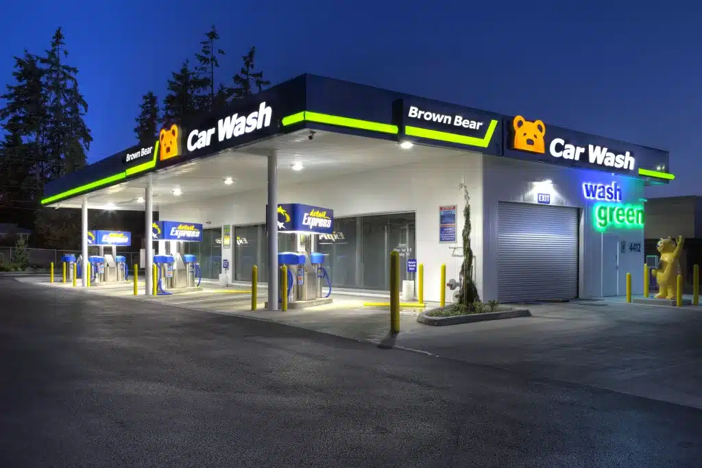 A car wash facility at night with bright lighting, featuring multiple washing bays and signage for "Brown Bear Car Wash.