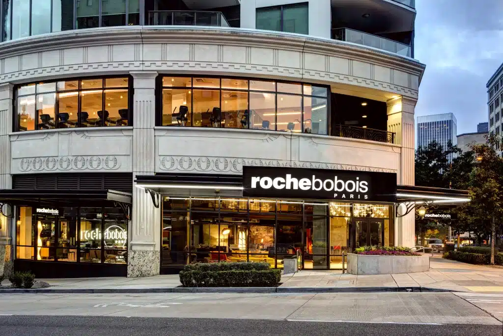 Street view of a Roche Bobois Paris furniture store with large windows and contemporary design, located on the corner of a building in an urban setting.