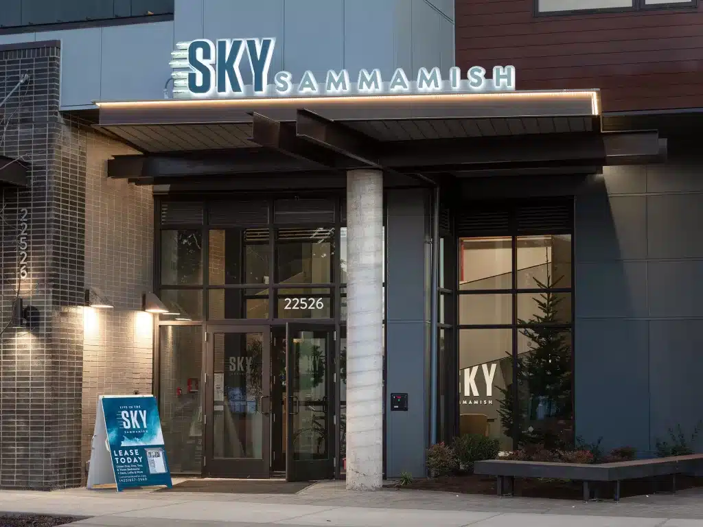 Entrance of Sky Sammamish building with glass doors, illuminated signage, and a leasing advertisement board outside.