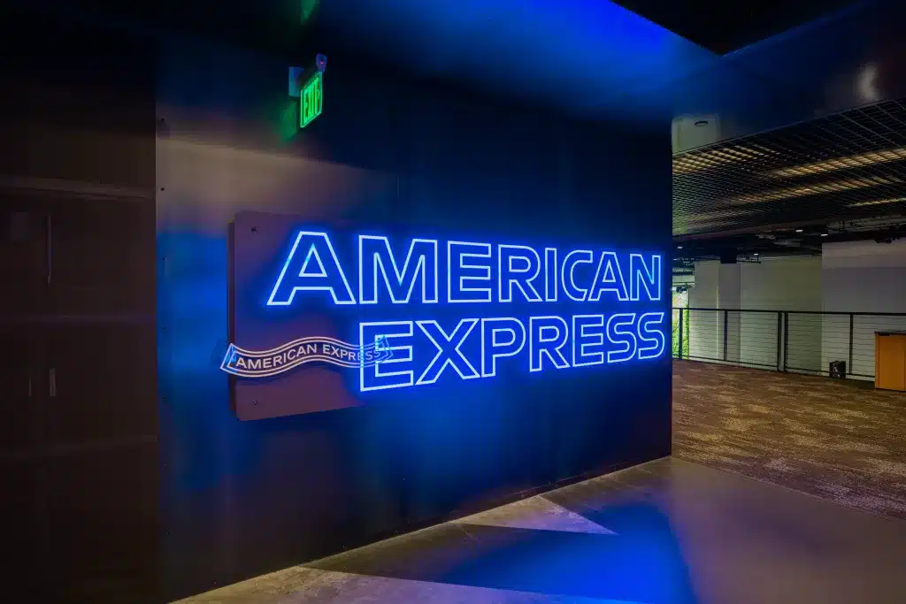 Neon-lit sign displaying "American Express" on a wall in a modern indoor setting.