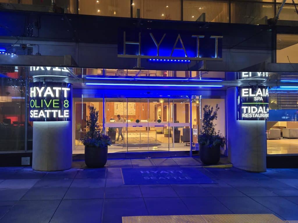 Entrance of a Hyatt hotel at night with illuminated signs for "Hyatt Olive 8 Seattle," "Elaia Spa," and "Tidal+ Restaurant.