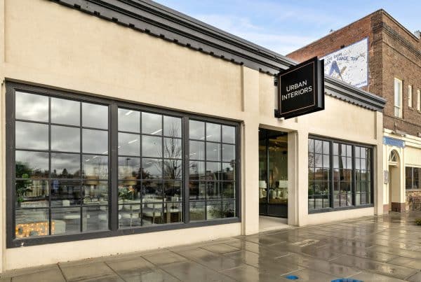 Storefront of Urban Interiors with large windows and a black sign. The exterior features beige walls and a sidewalk with a wet appearance.