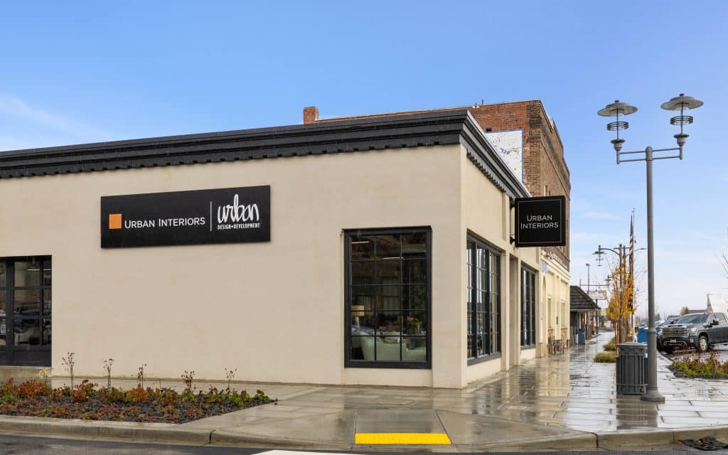 Street view of a building with "Urban Interiors" signs. The building features large windows and is situated on a wet sidewalk next to street lamps.